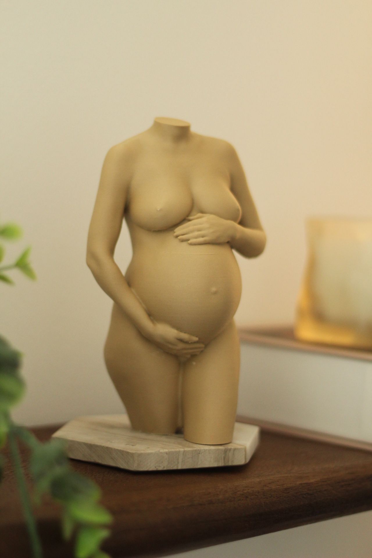 Klein beige beeldje van een zwangere vrouw op een houten plank, met de handen rustend op de buik.