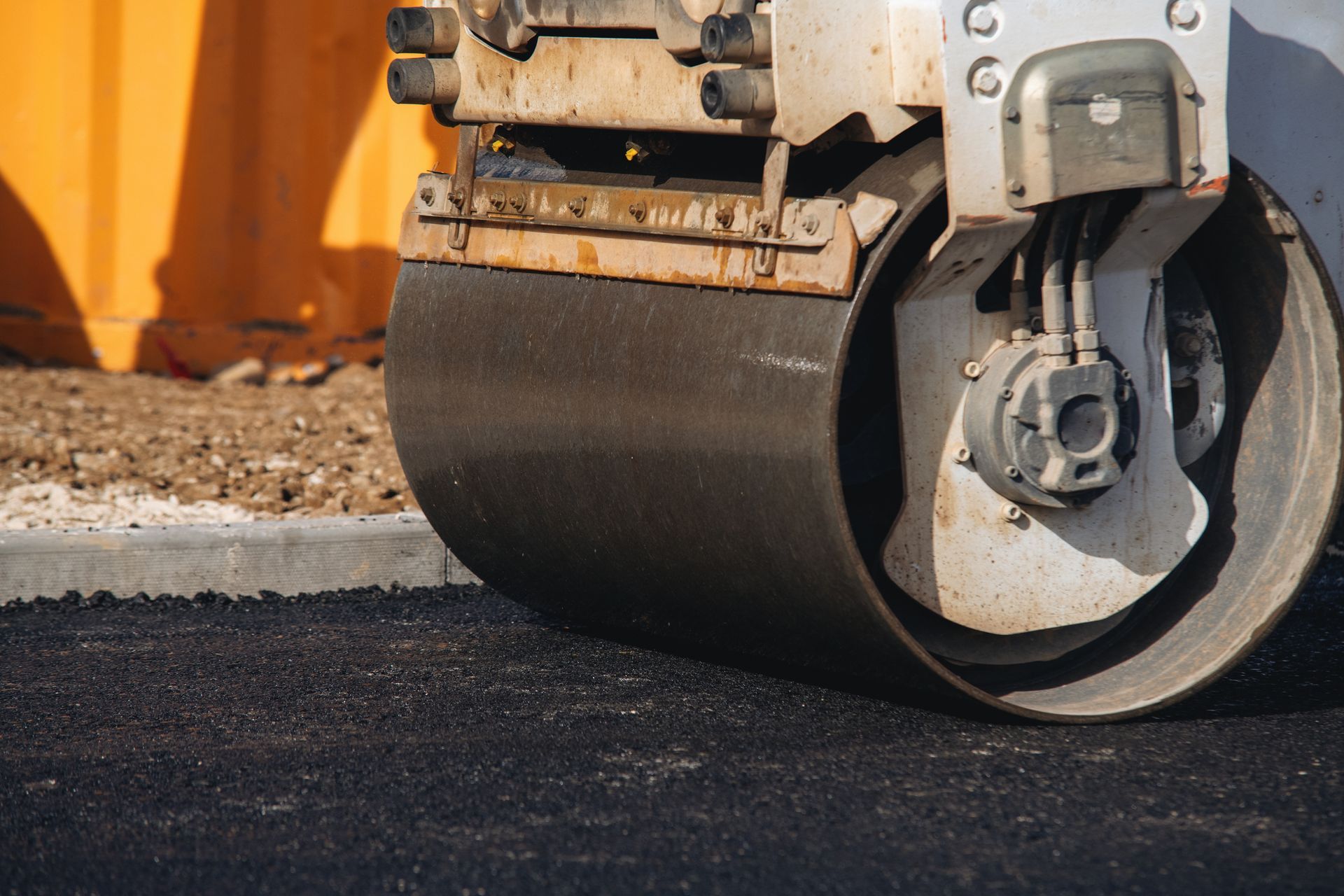 Close-up of a road roller's drum compacting freshly laid asphalt pavement.