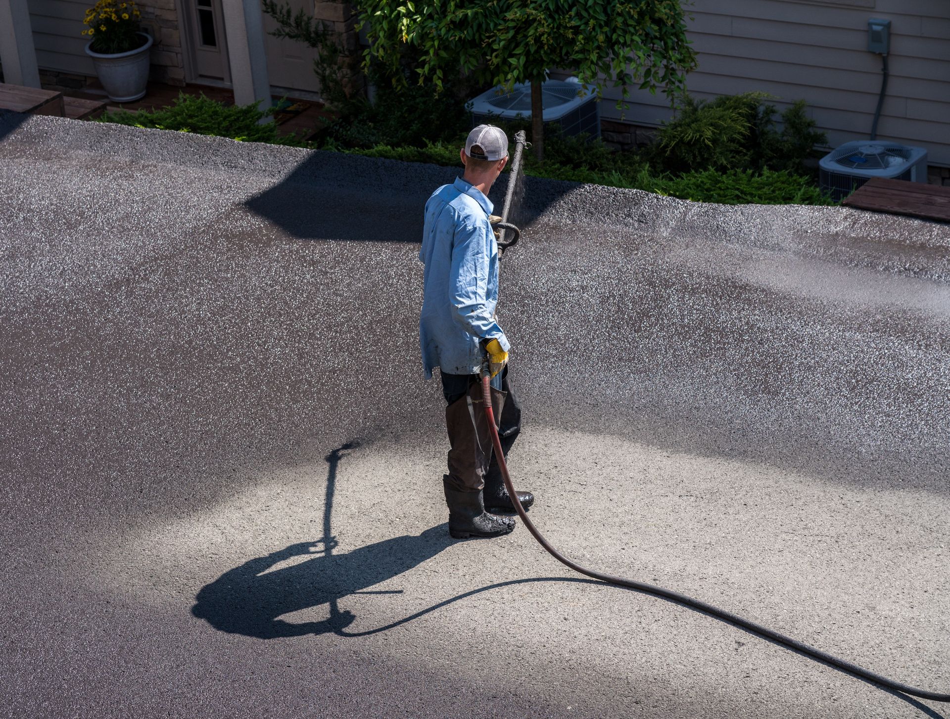 Driveway sealcoating contractor spraying protective coating on asphalt surface
