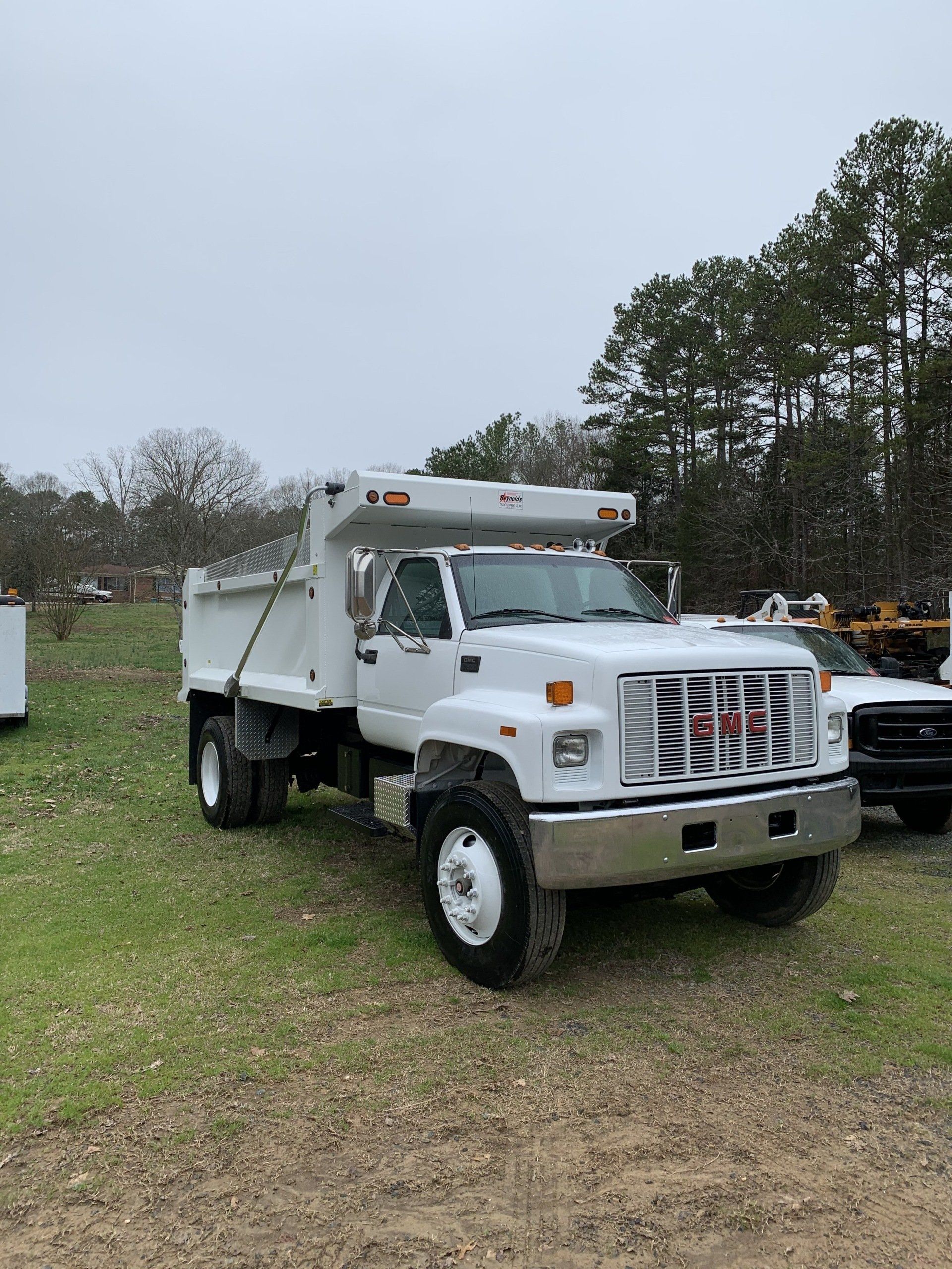 White GMC dump truck parked on grass, overcast day.