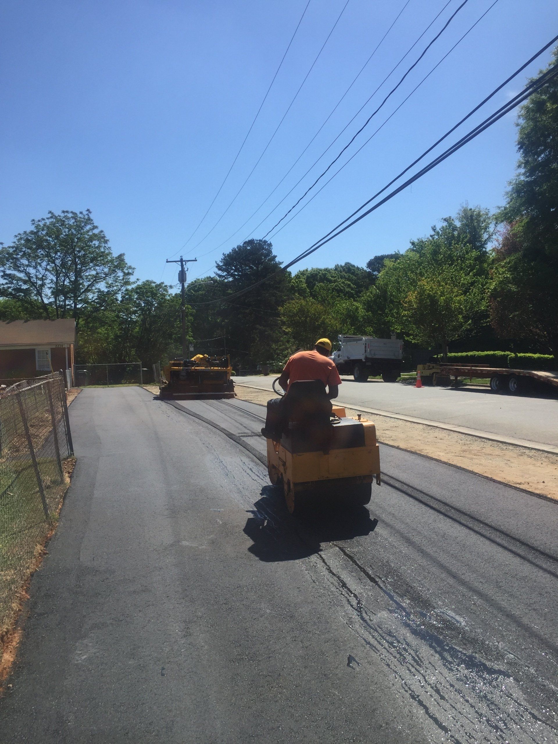 Asphalt paving in progress on a road. Workers use rollers and a machine to compact the new surface. Sunny day.