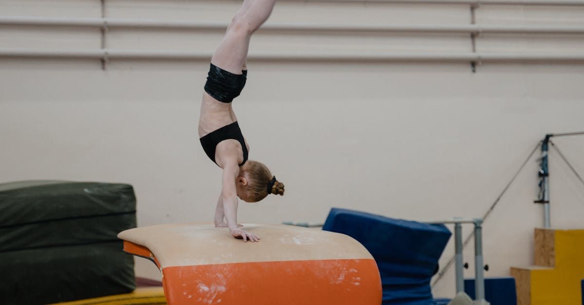 A young girl is doing a handstand on a balance beam in a gym.