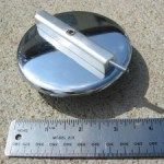 Chrome fuel cap with handle, next to a ruler, outdoors.