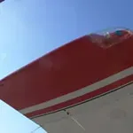 Red and white aircraft wing against a blue sky.