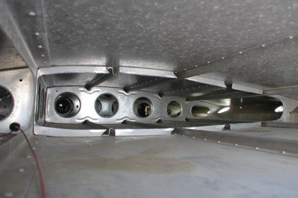 Interior view of an aircraft wing structure with multiple circular cutouts and support beams, all made of metal.