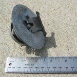 A gray, mechanical float assembly from a carburetor, next to a ruler for scale.