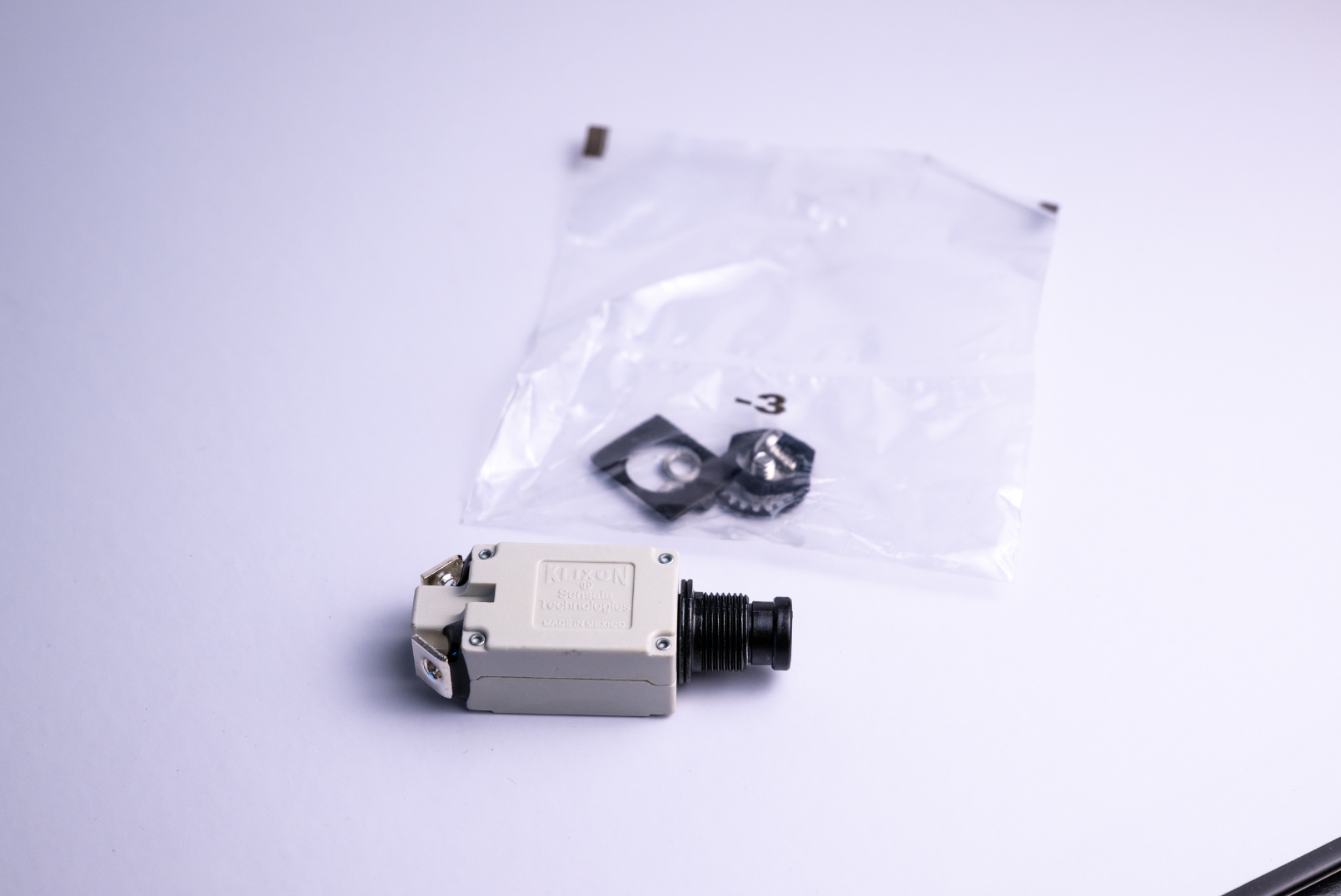 Camera and small parts in a plastic bag on a white surface.