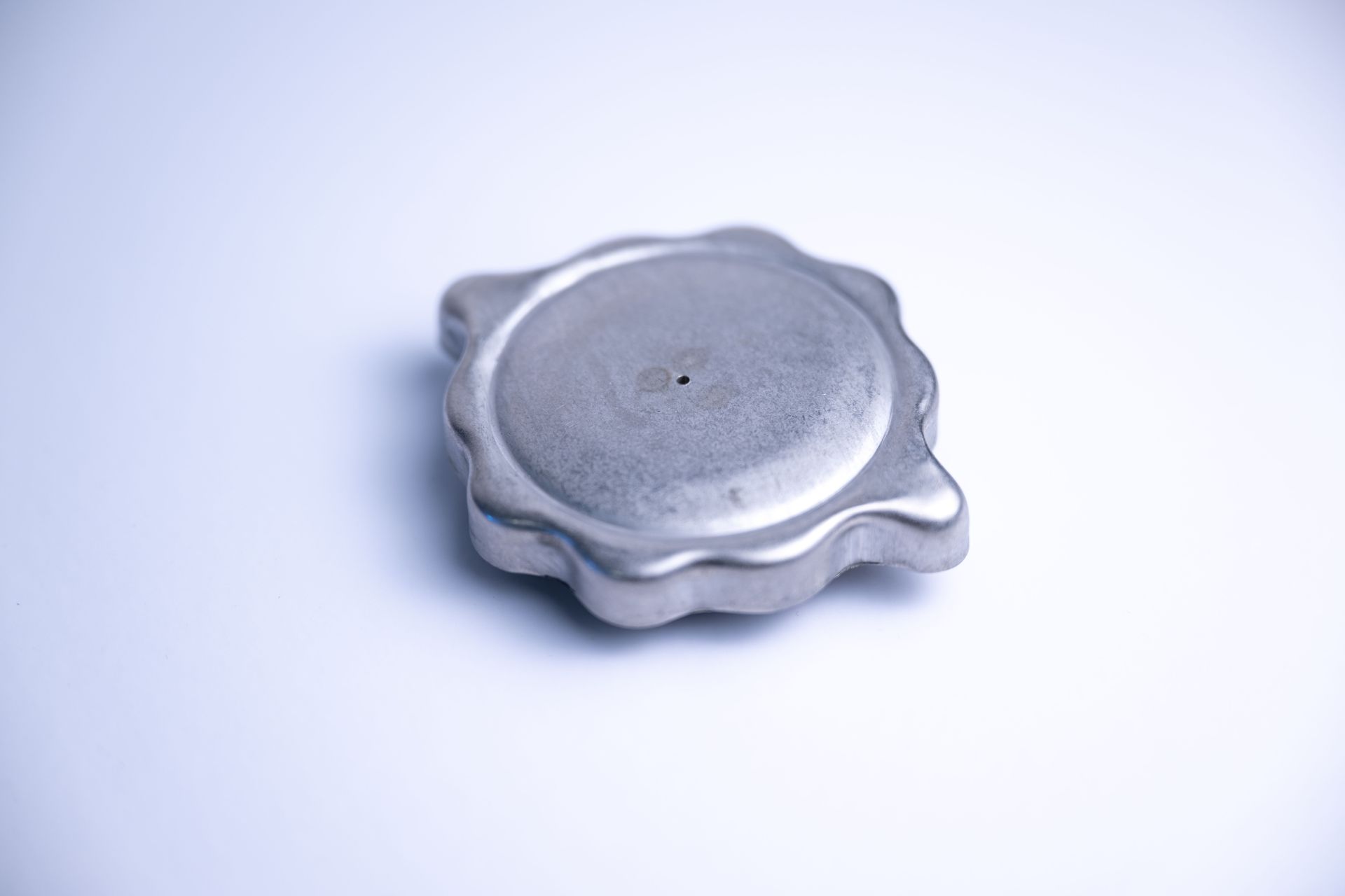Metal radiator cap with a circular top and a ridged edge, resting on a white surface.