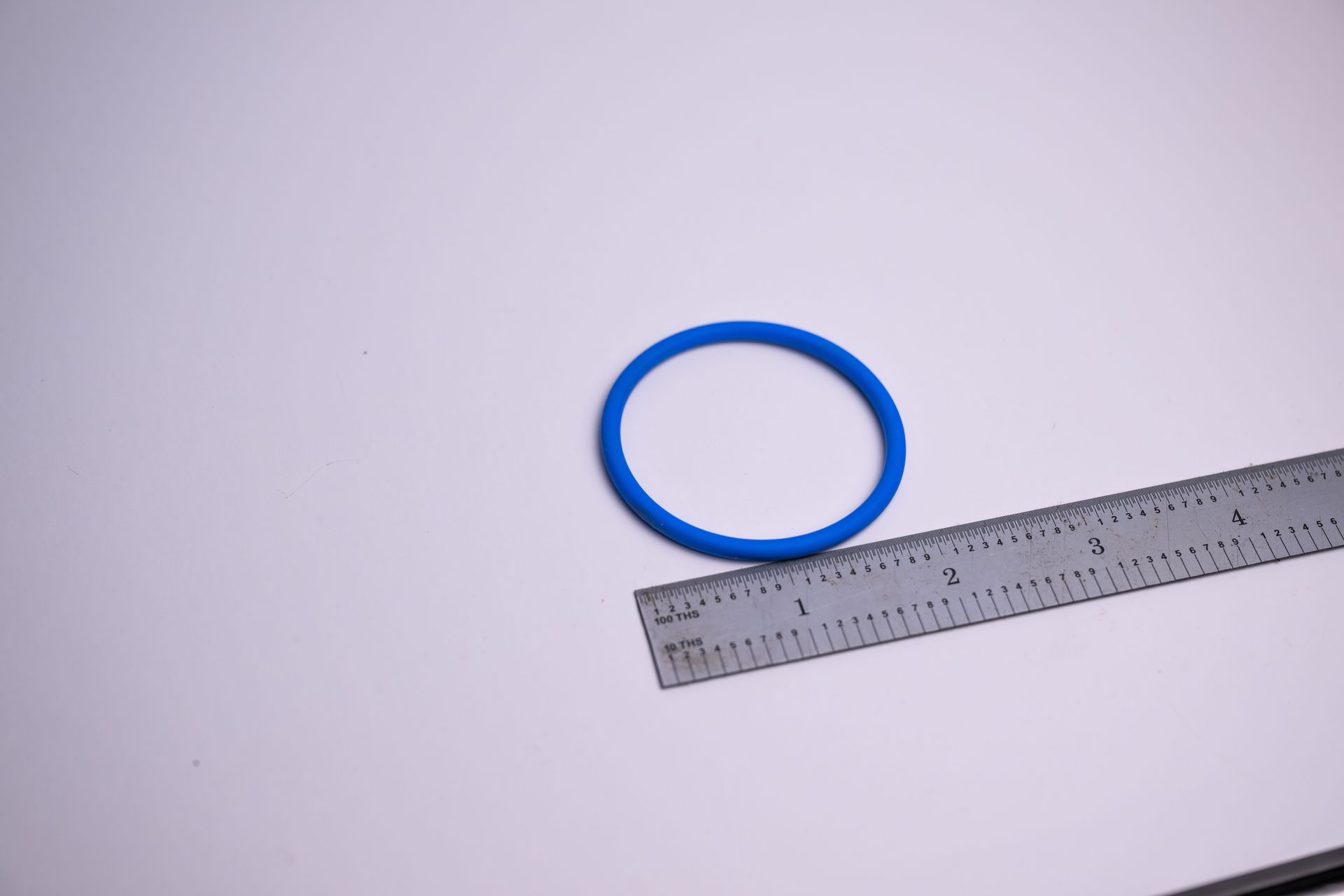 Blue circular rubber band next to a metal ruler on a white surface.