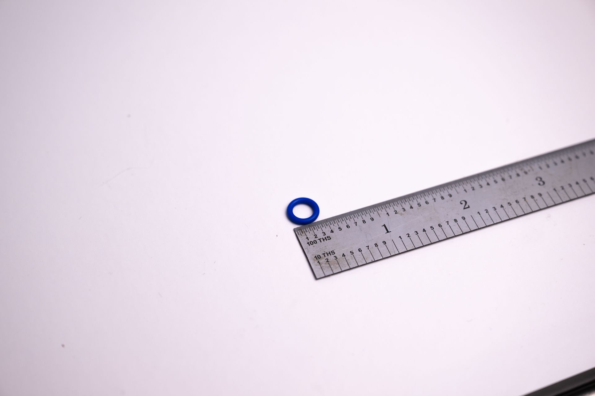 Blue O-ring next to a ruler on a white surface, showing size.