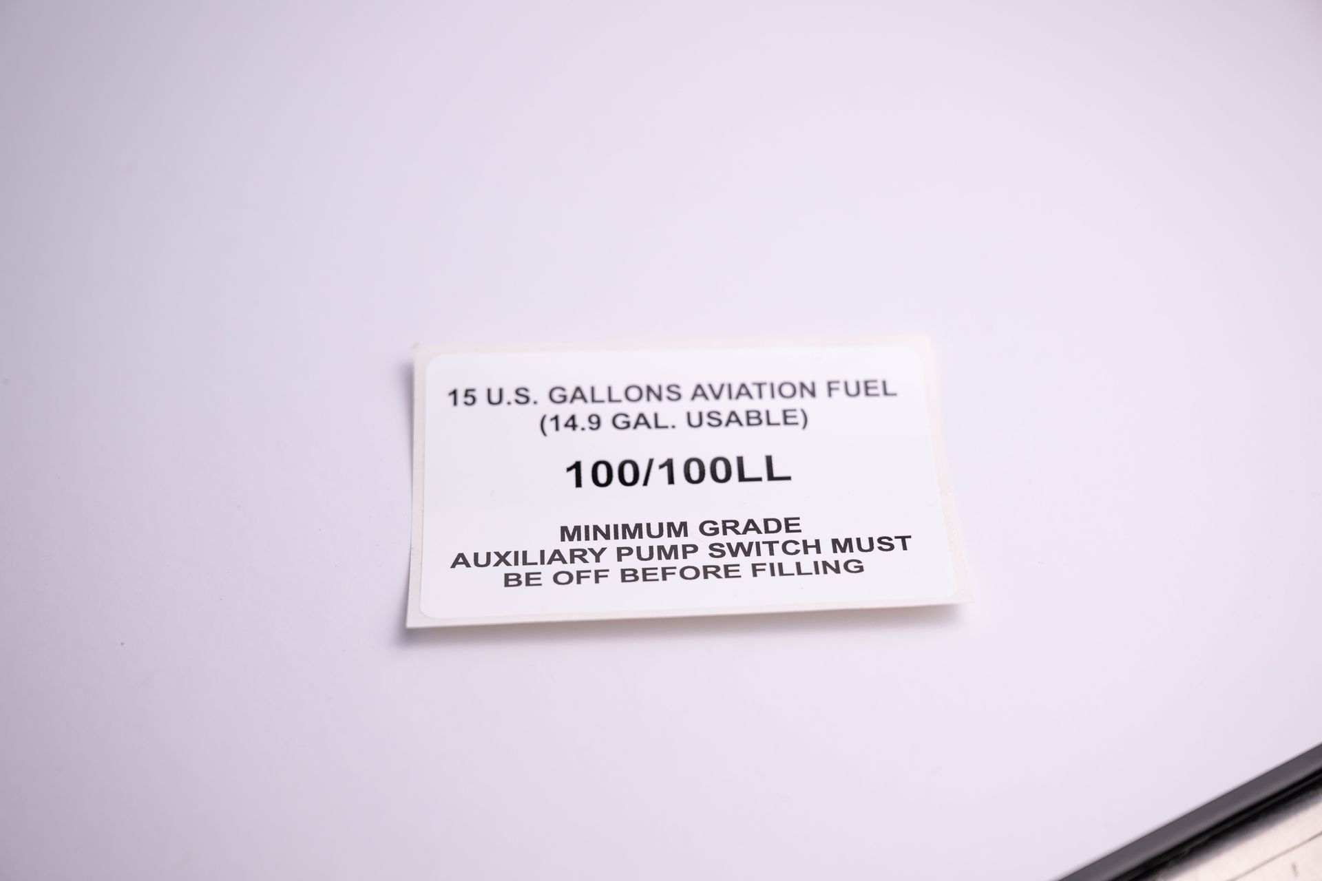 White label with text: 18 US Gallons Aviation Fuel, 100/100LL, minimum grade, aux fuel pump switch must be off before filling.
