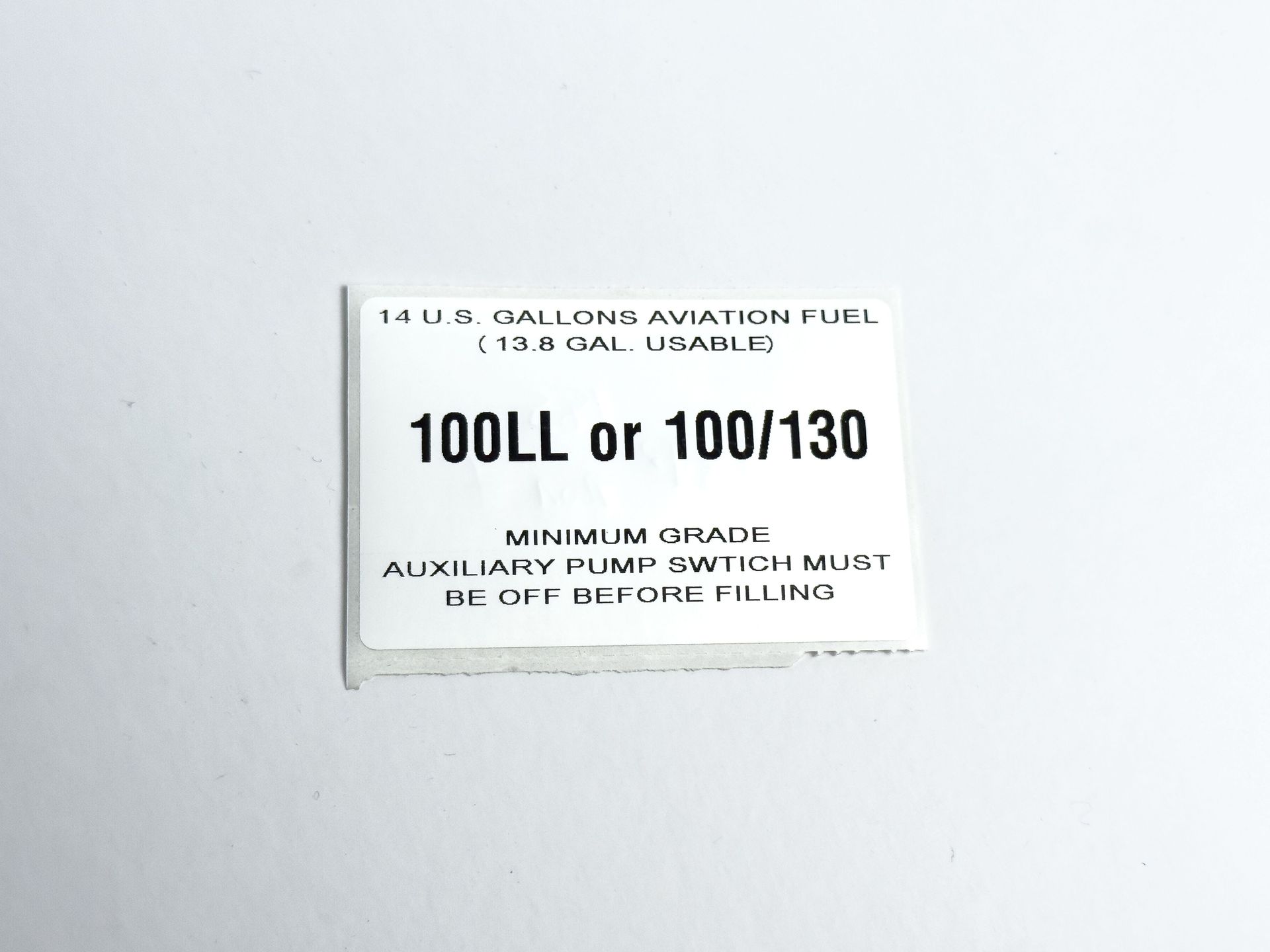 White fuel label with text indicating 100LL or 100/130 aviation fuel and instructions.