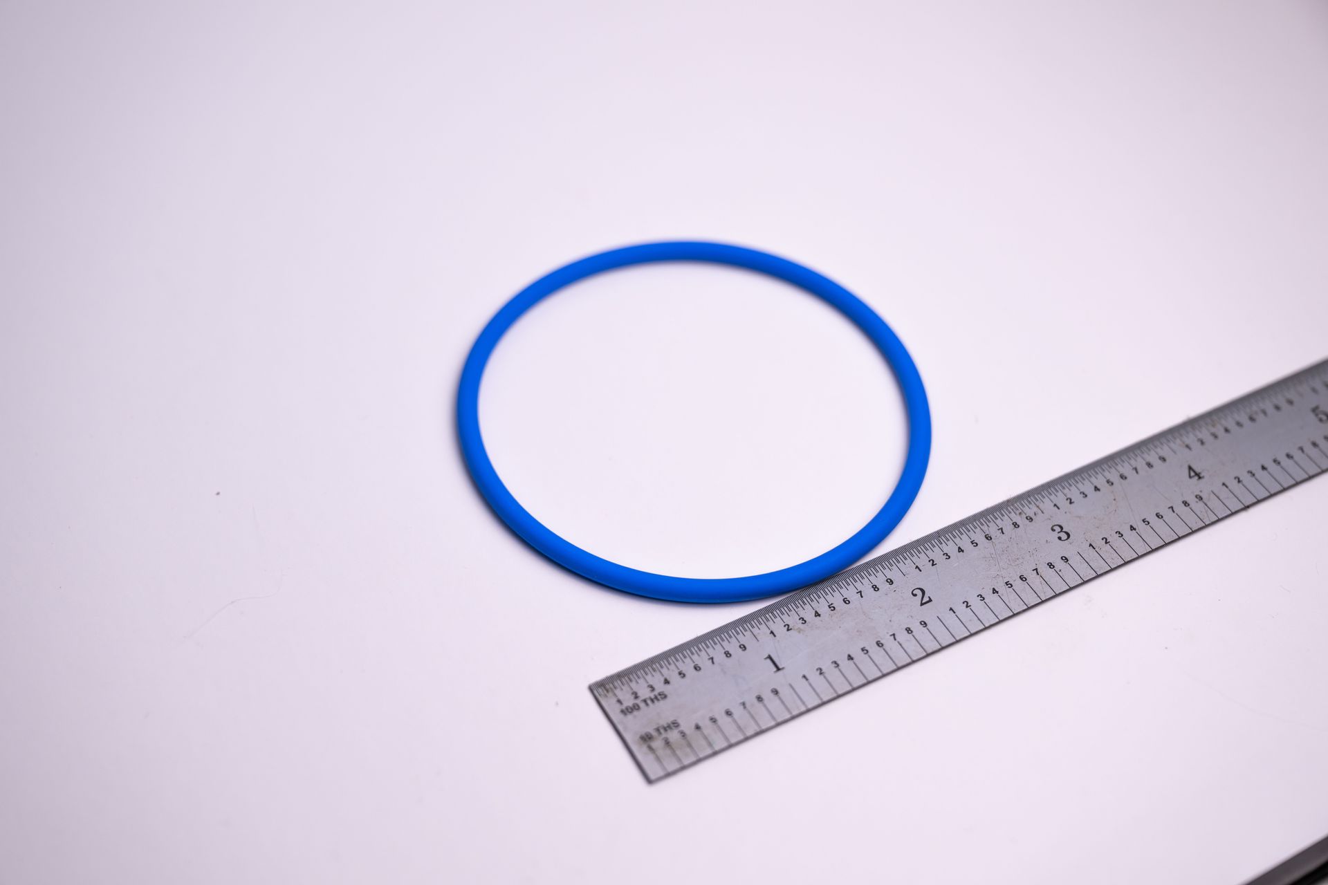 Blue rubber O-ring next to a ruler, set against a white background.
