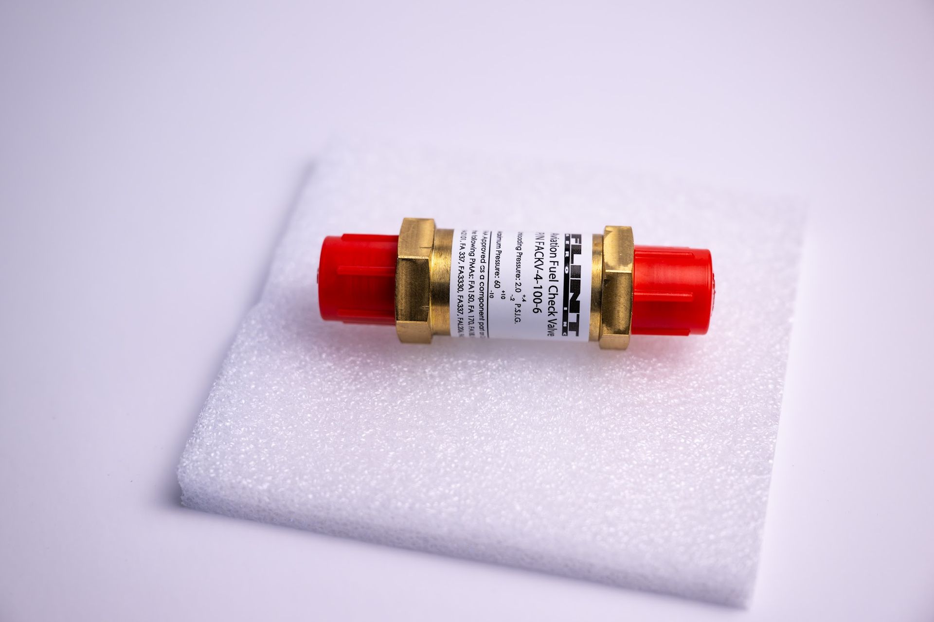 Red and brass fitting on white foam; product label visible.