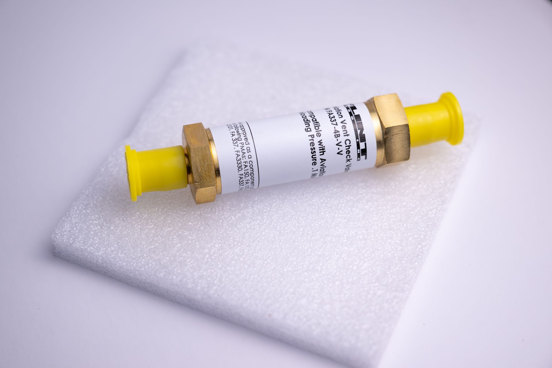 A cylindrical valve with brass fittings and yellow nozzles, on a white foam pad.