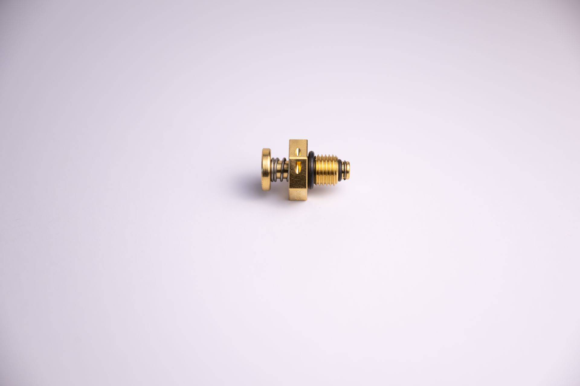 A small, brass-colored valve with spring components, resting on a white surface.