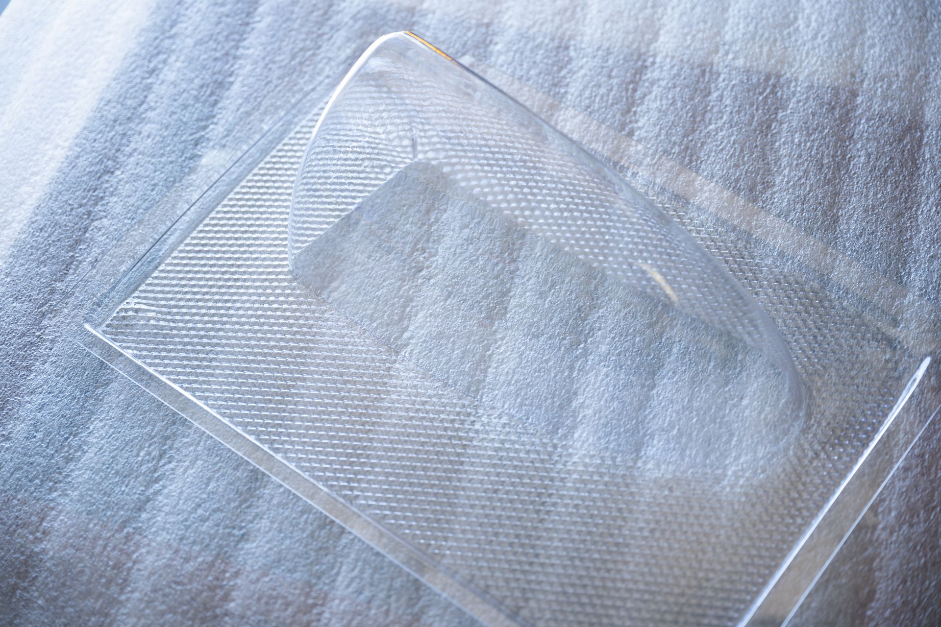 Clear acrylic display stand with a rounded top and a textured base, resting on a white, textured surface.
