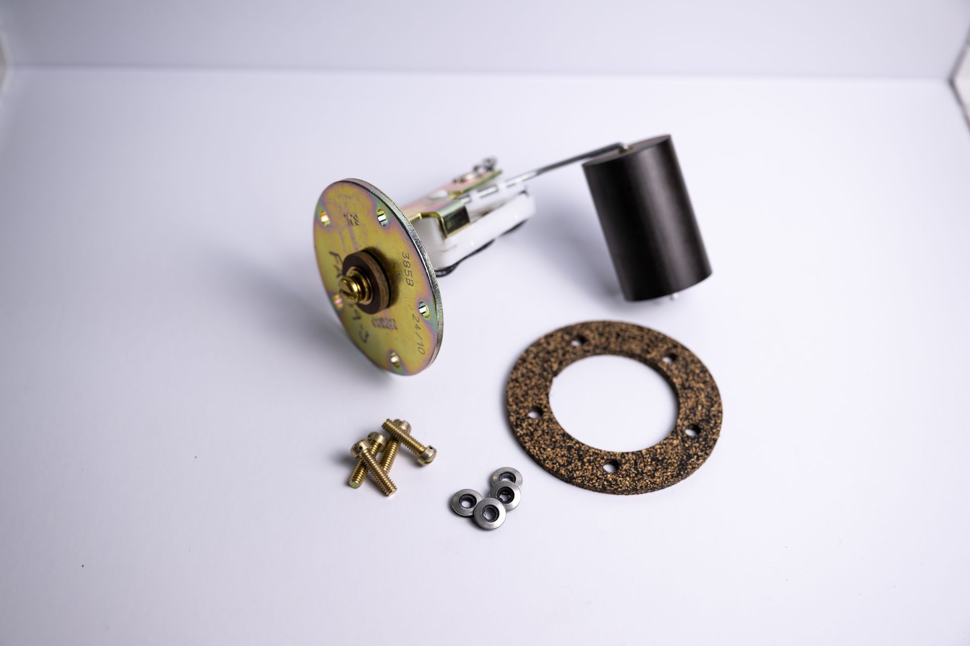 Fuel sending unit with mounting hardware and cork gasket, on a white surface.