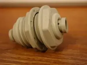 Gray plastic fitting with a ridged, conical body on a wooden surface.