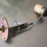 Fuel tank sending unit, metal arm with a cylindrical float and circular mounting plate.