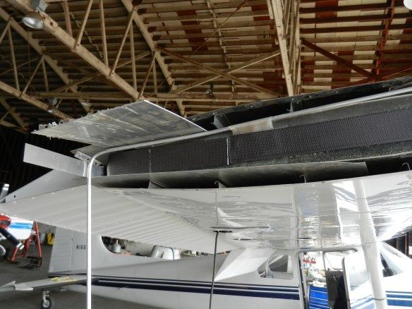 Damaged airplane wing with exposed internal structure, in a hangar.