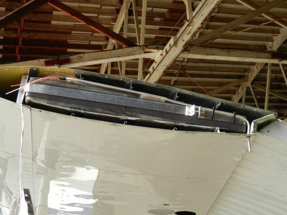 Close-up of a white aircraft wing with a dark-colored aerodynamic device attached, in a hangar.