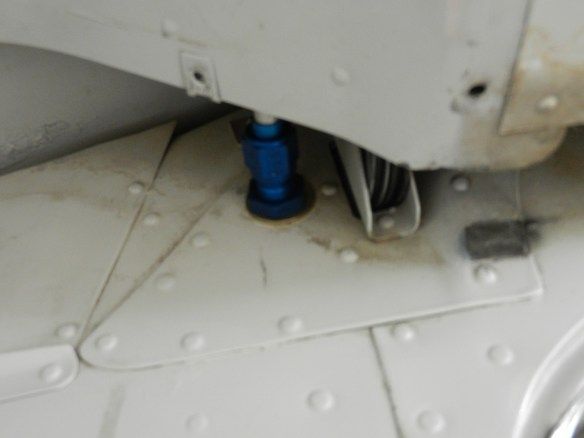 Blue aircraft jack point visible on white fuselage, surrounded by rivets and minor staining.