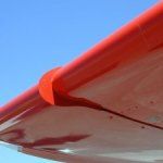 Red airplane wing against a blue sky, detail of the rounded wingtip and aileron.