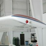 White aircraft wing in a hangar, with a red light, and a brown trim along the edge.