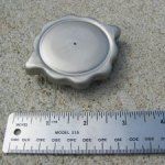 Silver metal cap with a scalloped edge next to a metal ruler, outdoors.