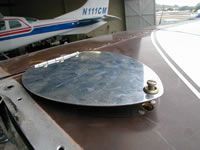 Metal access panel on the wing of a small airplane, partially obscuring the aircraft in the background.