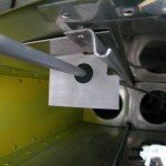 Aluminum bracket holding a gray rod, mounted on an aircraft's interior. Black rubber grommet visible.