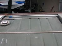 Overhead view of a gray tank with a fuel cap and metal bars, with a boat and garage in the background.