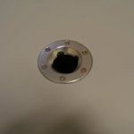 Metal cap with six holes, set in a light-colored surface. The opening is black.