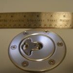 Silver fuel door with locking mechanism, a metal ruler is in the background.
