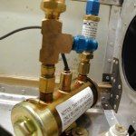 Close-up of brass and blue hydraulic pump components attached inside a metal aircraft frame.