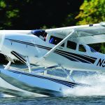 White seaplane with black stripes skimming across water, creating a wake.