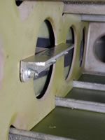 Metal bracket attached to an aircraft's internal structure with visible cutouts and rivets, viewed up close.