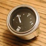 Fuel gauge showing just under 1/4 full, with a metal bezel, on a wood surface.