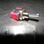 Red toggle switch next to a ruler, set against a dark surface.
