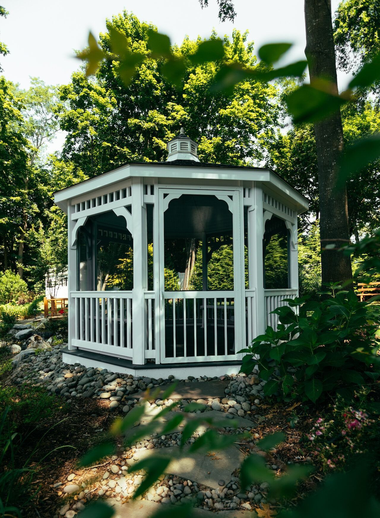 Two light-colored Adirondack chairs with a shared table sit on a lush lawn near a metal armillary sphere garden ornament.