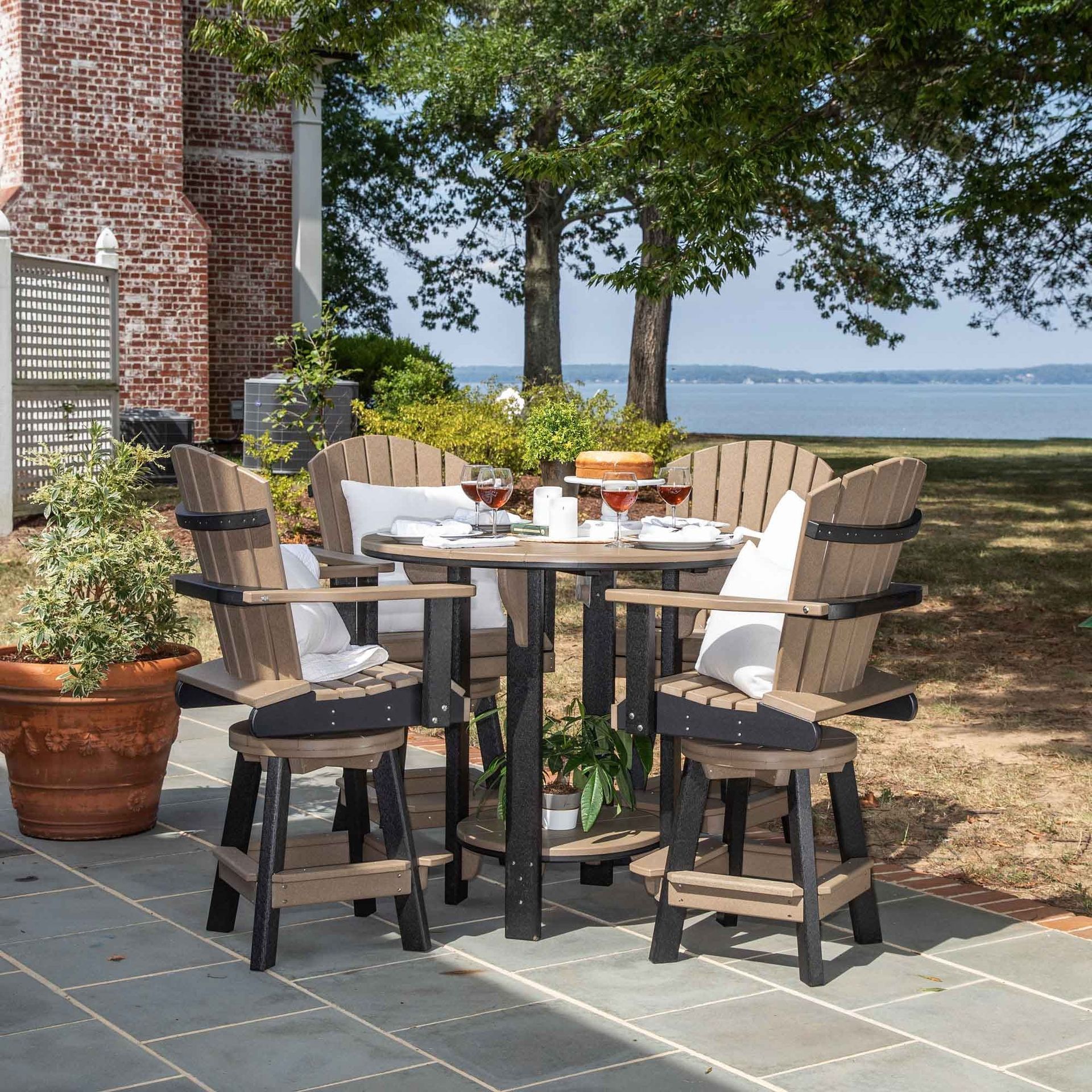 Two light-colored Adirondack chairs with a shared table sit on a lush lawn near a metal armillary sphere garden ornament.