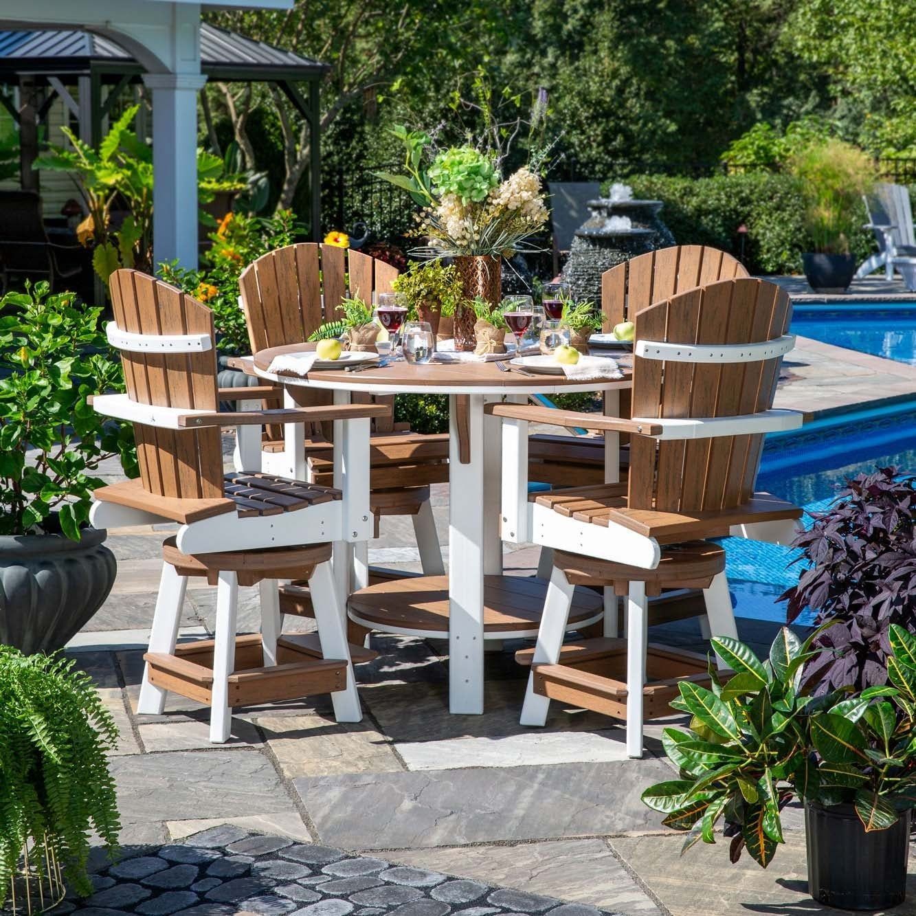 Outdoor patio table set beside a blue pool, surrounded by wooden chairs and lush greenery