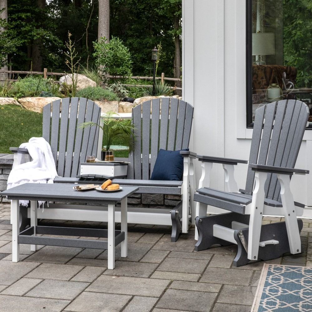 Cozy outdoor patio with wooden chairs, round table, flowers, and food beside a house and garden greenery