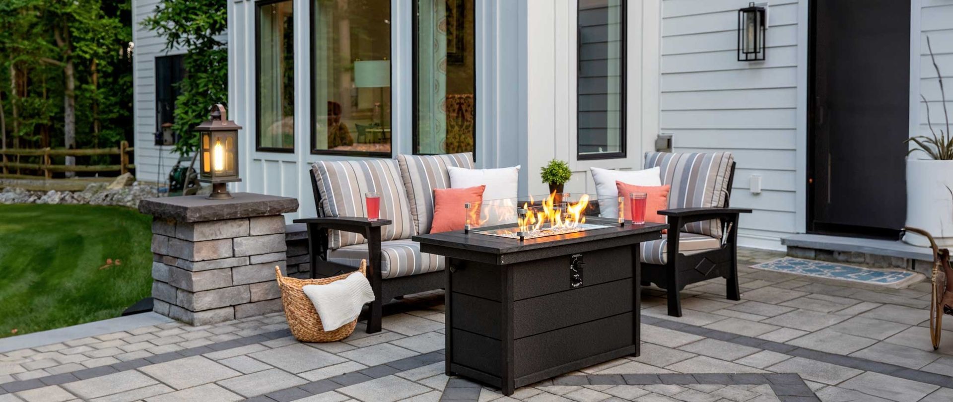 Patio seating area with cushioned chairs, fire pit table, and lanterns beside a house