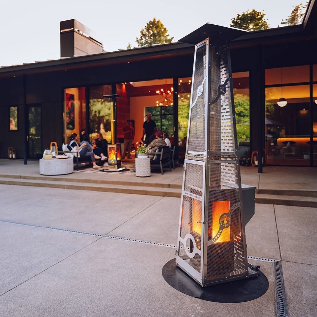 Outdoor café patio with a tall metal heater in front of a modern restaurant at dusk