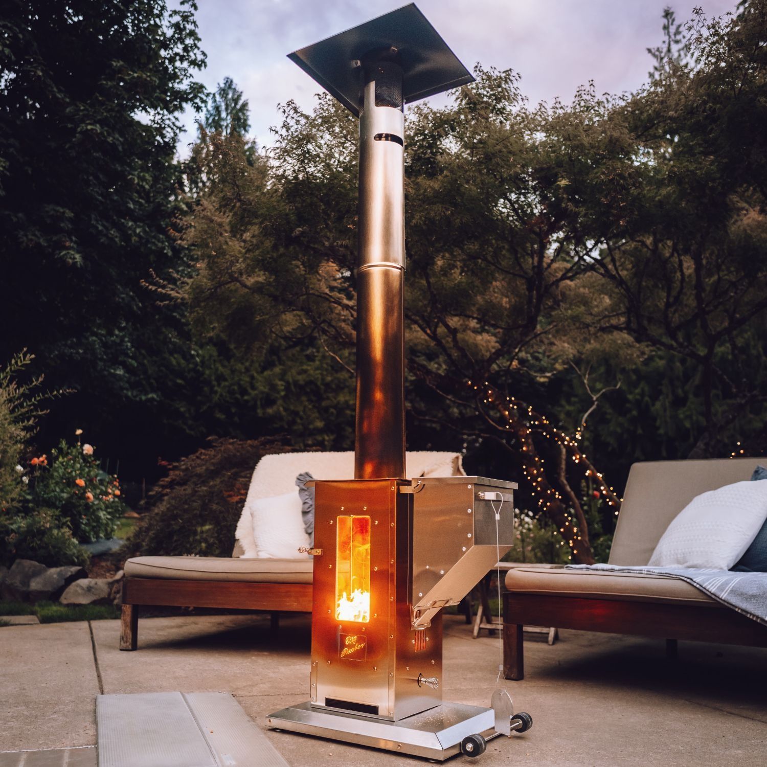 A tabletop fire pit with a single, flickering flame inside a clear cylindrical glass shield, set on a dark wood table.