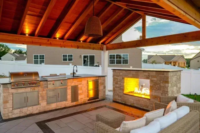 A patio features a bright green outdoor sofa, a dark wooden side table with potted plants, and a white, shingled wall.