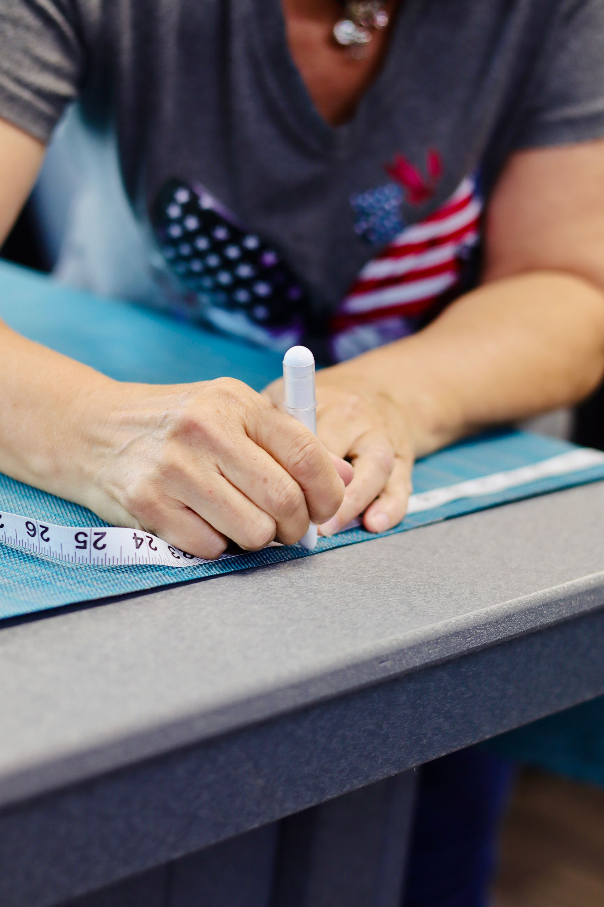 Hands marking fabric with a chalk pencil beside a measuring tape on a worktable