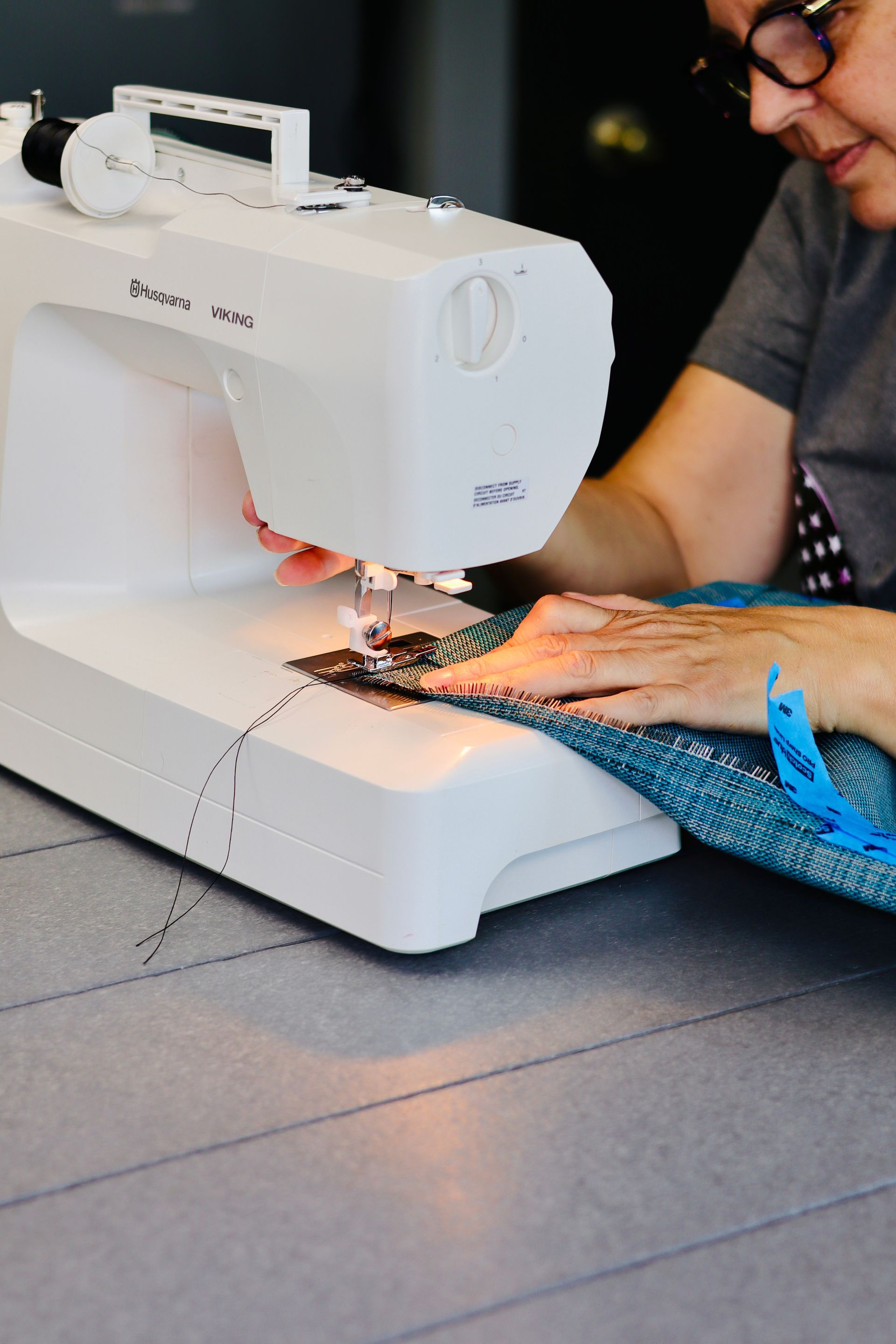 Person sewing blue fabric with a white sewing machine at a table